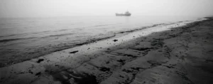 Orilla del mar con una mancha de petróleo y un buque en el horizonte.