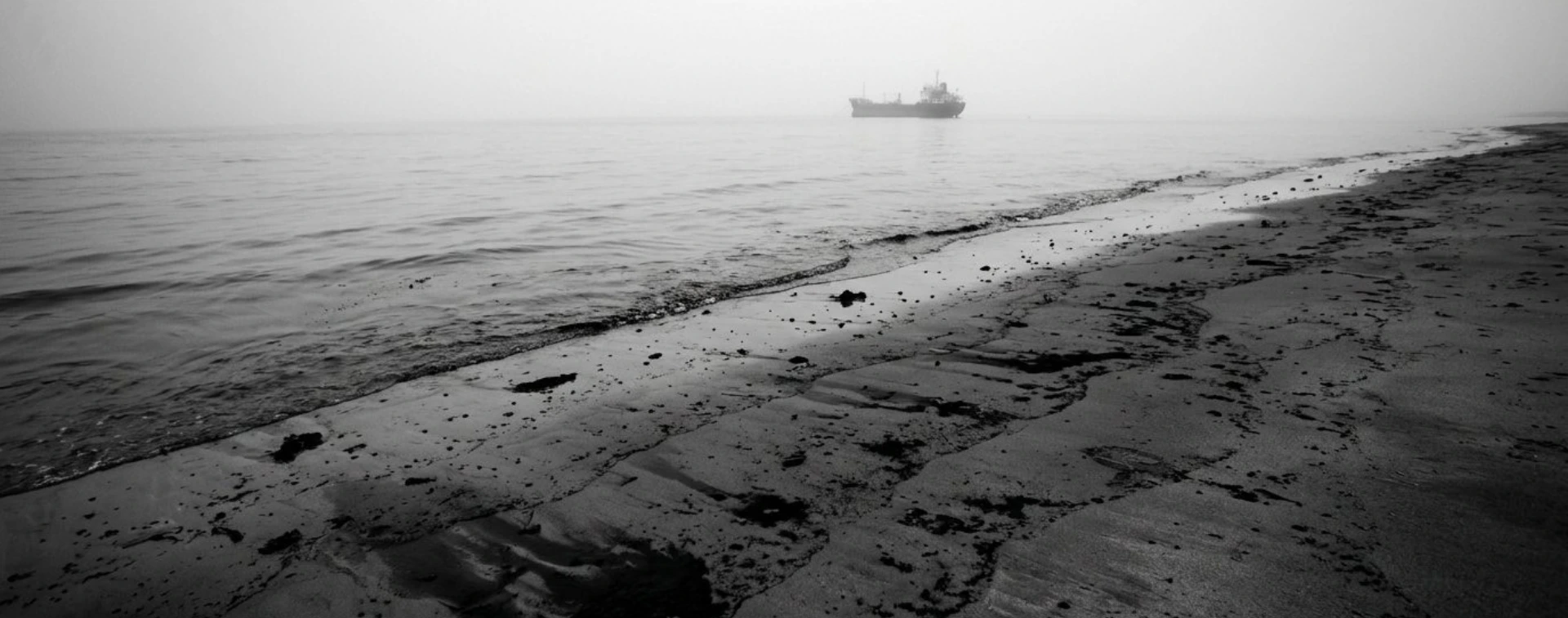 Orilla del mar con una mancha de petróleo y un buque en el horizonte.