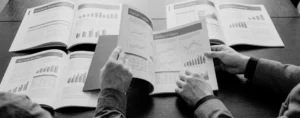 Manos sosteniendo informes impresos abiertos en páginas de gráficos financieros.