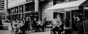 Terraza de un café con personas conversando y alguien leyendo el diario.