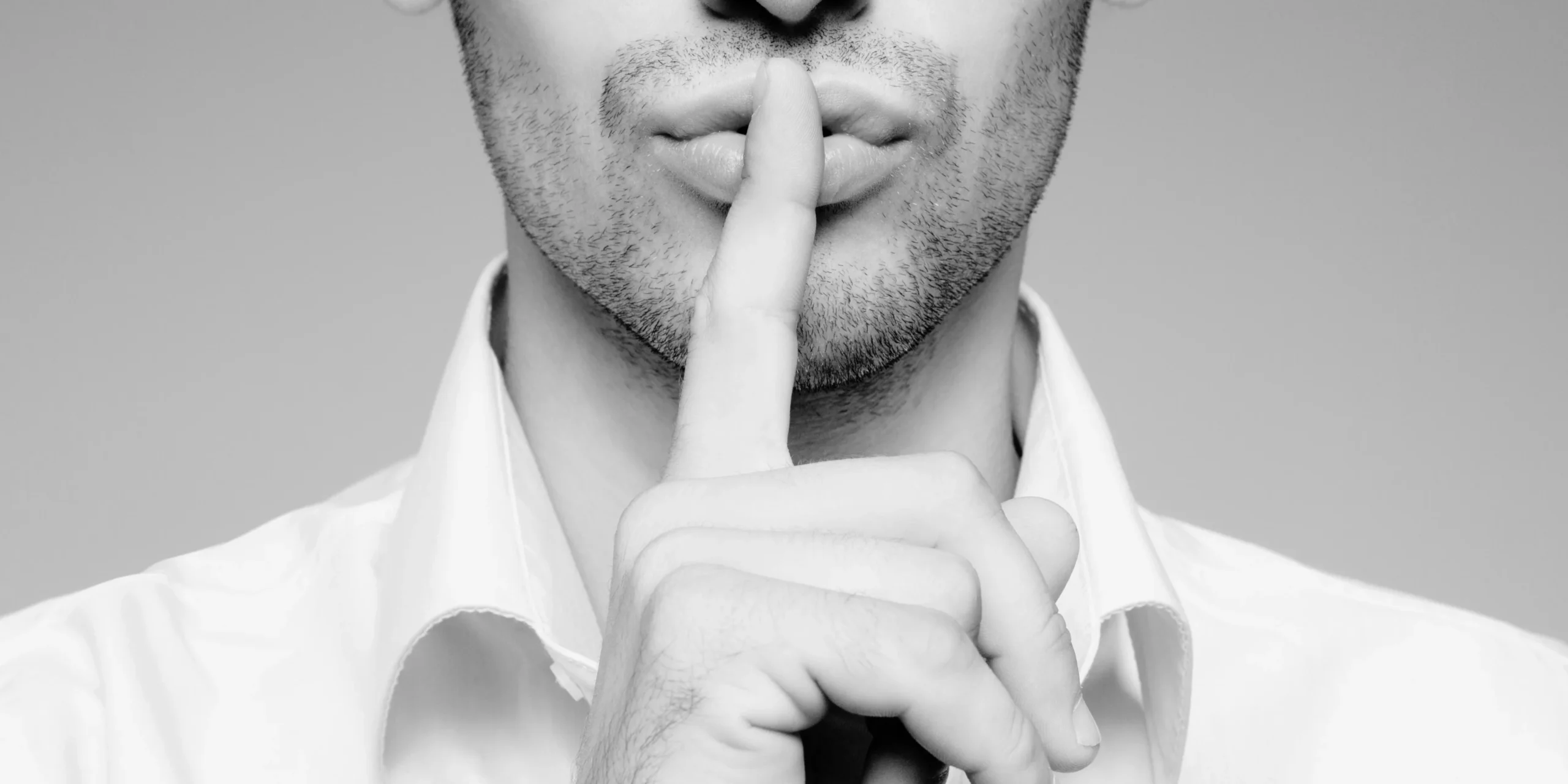 Hombre con el dedo índice sobre los labios pidiendo silencio.
